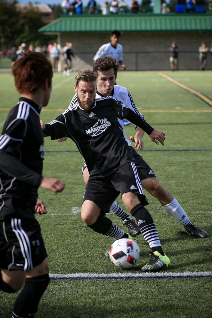 Photo of a soccer player controlling the ball with a defender on his back.